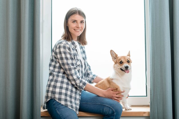 smiley woman posing with her dog in front of window