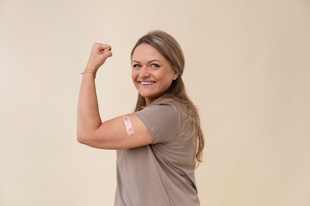 Free photo smiley woman showing bicep with sticker after getting a vaccine