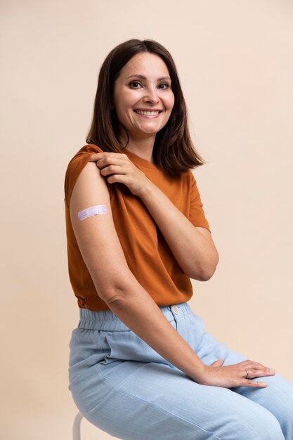 Улыбающаяся женщина показывает наклейку на руке после вакцинации