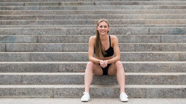 Smiley woman sitting on stairs long shot