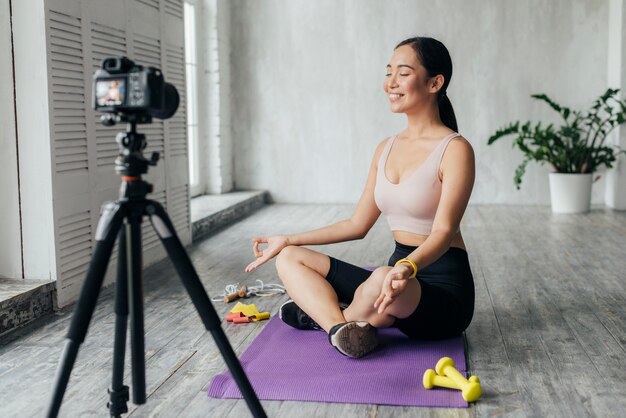 Smiley woman in sportswear vlogging while meditating