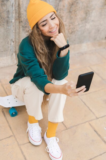 Smiley woman taking selfie while sitting on skateboard