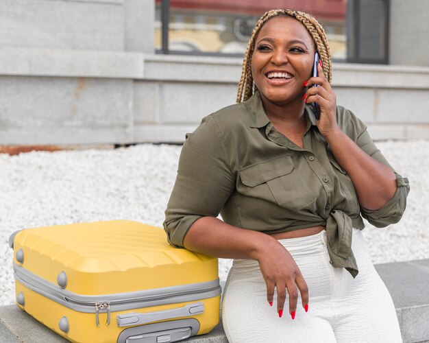 Smiley woman talking on the phone next to her yellow luggage