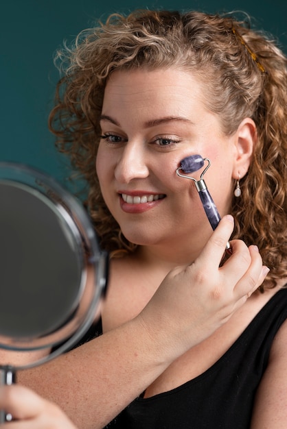 Smiley woman using gua sha tool and mirror