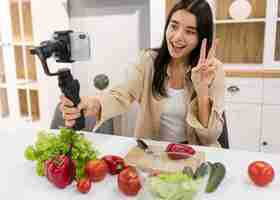 Foto gratuita donna di smiley vlogging a casa con verdure e smartphone