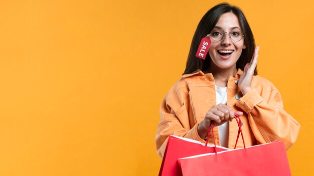 Smiley woman wearing glasses with sale tag and holding shopping bags