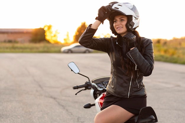 彼女のバイクに座っているヘルメットを持つスマイリー女性