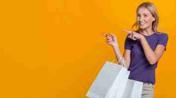 Foto gratuita donna sorridente con molte borse della spesa che punta al possibile negozio con copia spazio