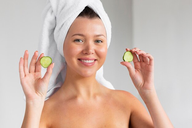 Smiley woman with towel on head holding cucumber slices