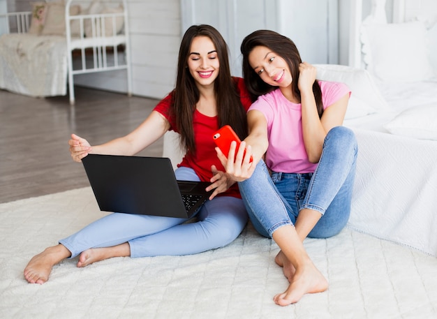 Donne di smiley che si siedono sul pavimento e che prendono selfie