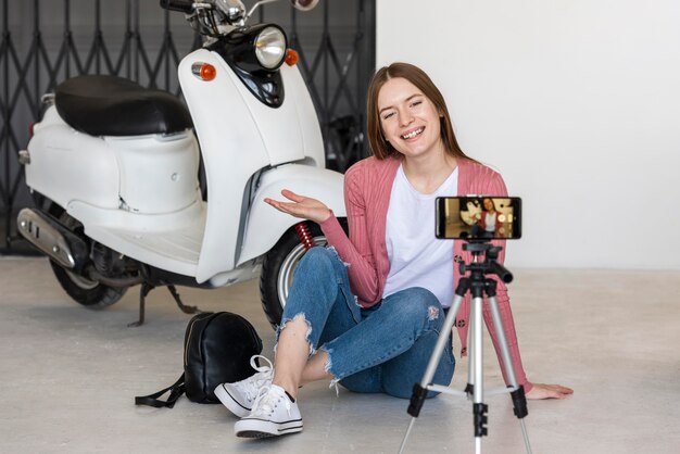 自分のバイクの隣に座って自分自身を記録するスマイリーの若いブロガー