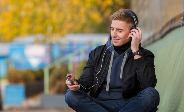 Smiley young man listening to music on headphones on a bench