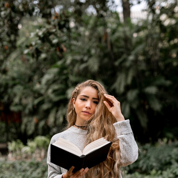 Smiley young woman holding a book outdoors