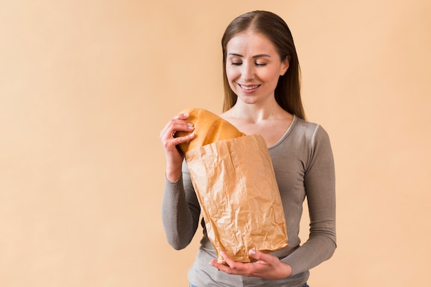 Smiley young woman holding paper bag with bread