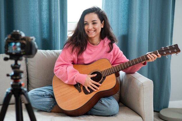 Smiley young woman playing guitar on camera