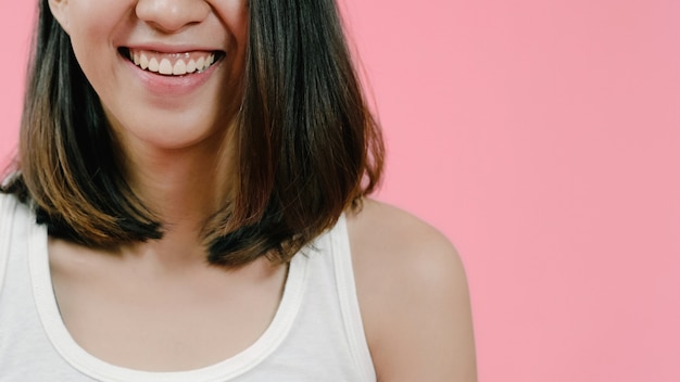 Foto gratuita la femmina asiatica adorabile sorridente con l'espressione positiva, sorride largamente, si è vestita in abbigliamento casuale e sta esaminando la macchina fotografica sopra fondo rosa.