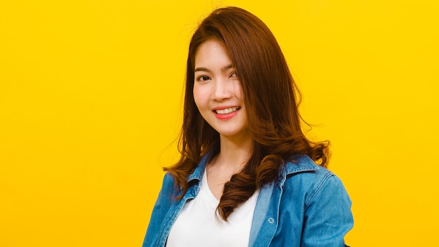 Smiling adorable Asian female with positive expression, smiles broadly, dressed in casual clothing and looking at the camera over yellow wall. Happy adorable glad woman rejoices success.