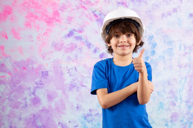 улыбающийся прелестный мальчик в синей футболке и белом шлеме на разноцветном