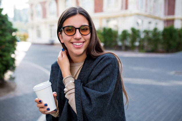 Smiling adorable shy woman walking with coffee on the street and enjoys weekend in the city