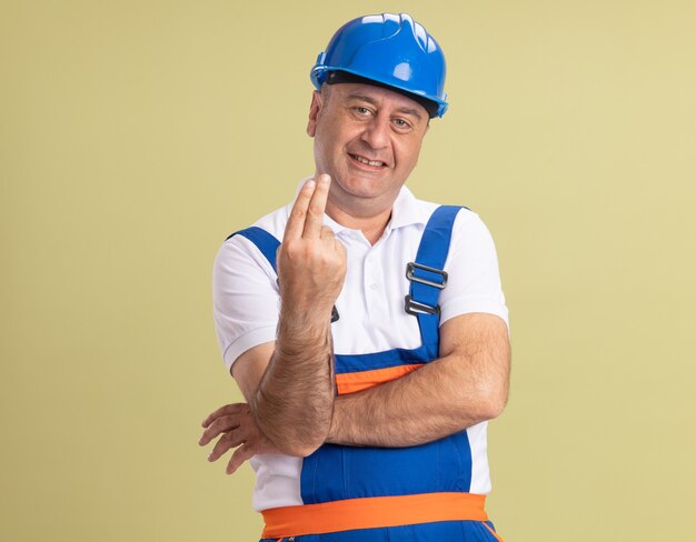 Smiling adult builder man in uniform gestures two with fingers on olive green