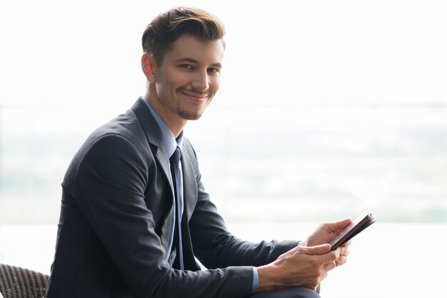 Smiling Adult Businessman Sitting and Using Tablet