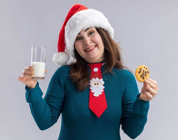 산타 모자와 산타 넥타이와 웃는 성인 백인 여자 보유 우유와 쿠키 복사 공간 흰색 배경에 고립의 유리
