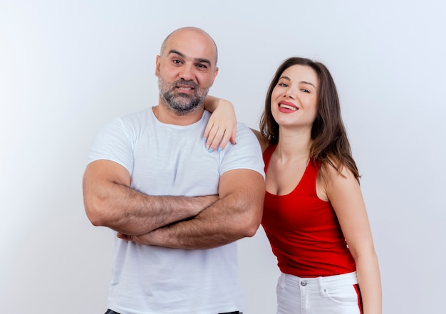 Smiling adult couple man standing with closed posture and woman putting hand on his shoulder both looking 