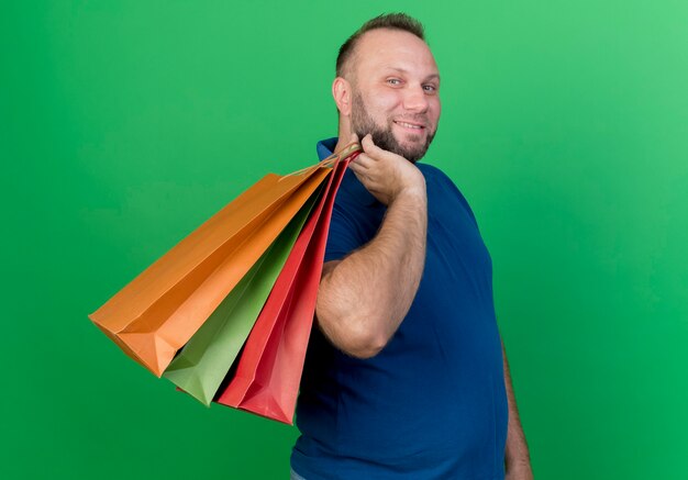 Free photo smiling adult slavic man holding shopping bags on shoulder looking isolated