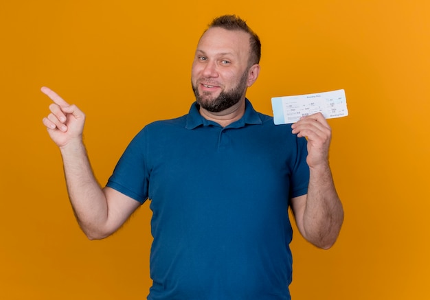 Smiling adult slavic man holding travel ticket looking pointing at side