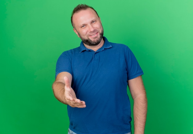 Foto gratuita uomo slavo adulto sorridente che allunga la mano che fa ciao gesto isolato sulla parete verde con lo spazio della copia
