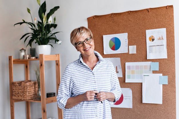 Foto gratuita sorridente donna adulta in occhiali pone in ufficio