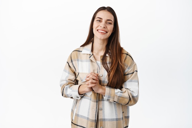 Smiling adult woman say thank you, look pleased and grateful for help, holding hands together near chest, standing happy against white background