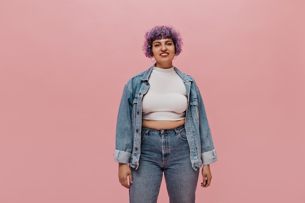 Free photo smiling adult woman with short curly purple hair in white top, in denim jacket and tight jeans posing.