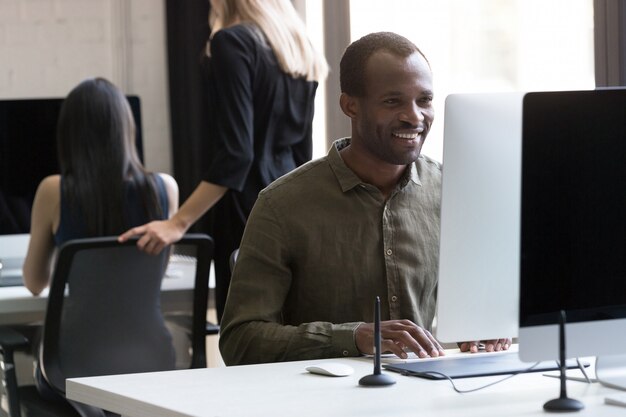 彼のコンピューターに取り組んでいる笑顔のアフリカ系アメリカ人実業家