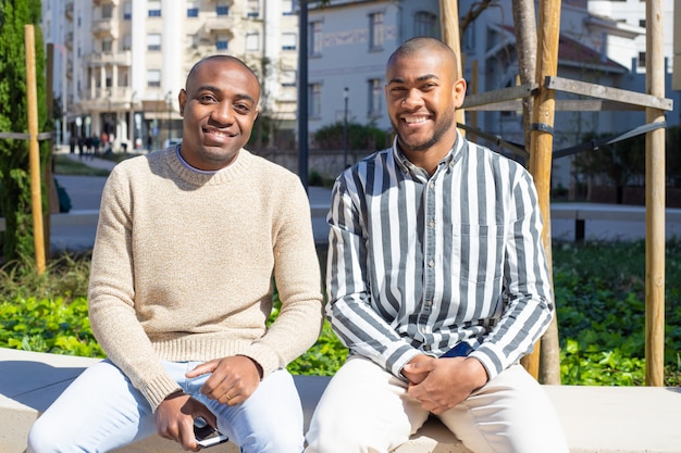 Улыбающиеся афро-американские парни сидят на скамейке с телефонами