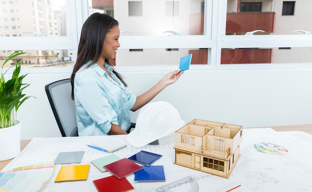 Smiling African-American lady on chair near plan and model of house on table