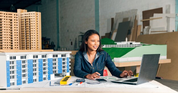 휴대용 퍼스널 컴퓨터와 건물의 모델 웃는 아프리카 계 미국인 여자