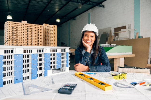 Foto gratuita donna afroamericana sorridente nel casco di sicurezza vicino al modello di costruzione