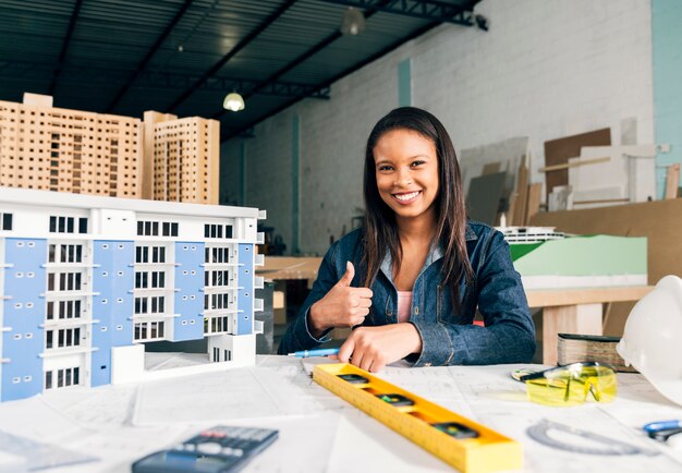 Smiling African-American woman showing thumb up near model of building
