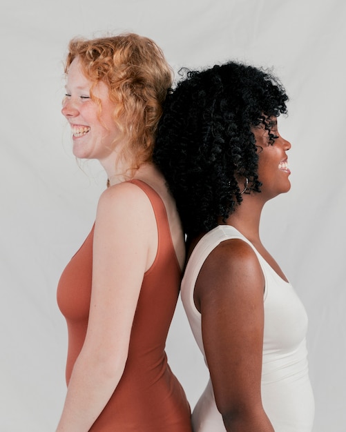 Free photo smiling african and blonde young women standing back to back standing against grey backdrop