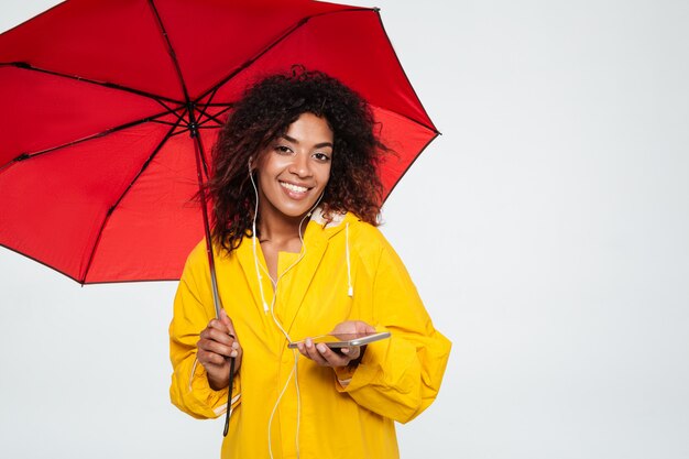 傘の下に隠れて音楽を聴くのレインコートでアフリカの女性を笑顔