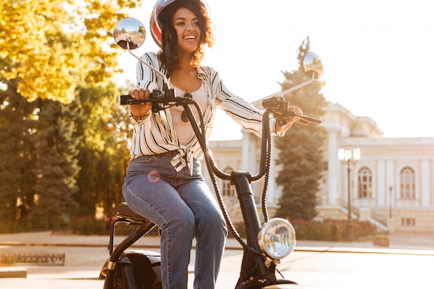 Улыбается африканская женщина, сидя на современном мотоцикле на открытом воздухе