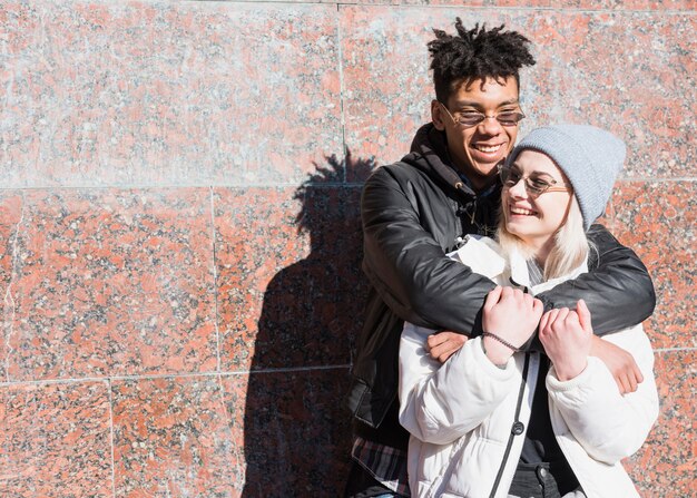 Smiling african young man standing against wall hugging her girlfriend