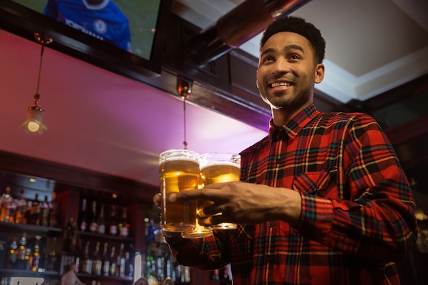 Free photo smiling afro american man carrying glasses of beer