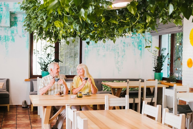 Smiling aged couple sitting in cafe with mugs of tea