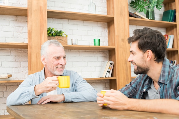 Smiling aged man and happy young guy with cups at table