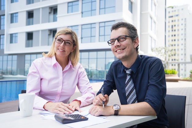 Free photo smiling ambitious accountants sitting at table with papers and calculator