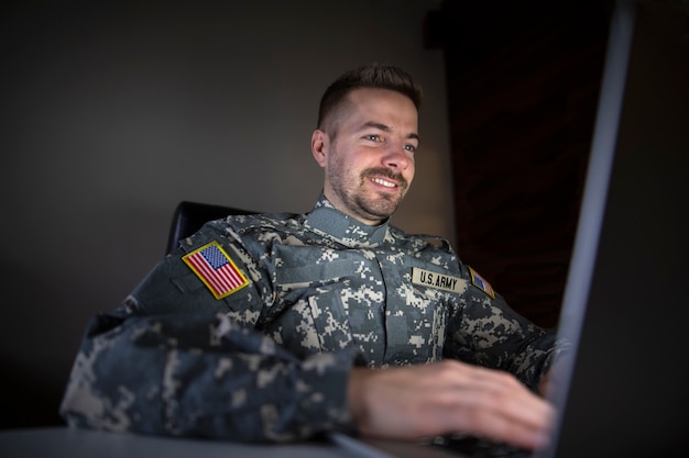 Smiling american soldier with USA patch flag using laptop computer