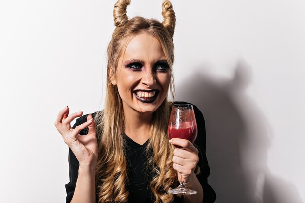 파티를 즐기는 뱀파이어 의상 매력적인 아가씨 미소. 와인 글라스에 가짜 혈액과 웃는 여자의 사진.