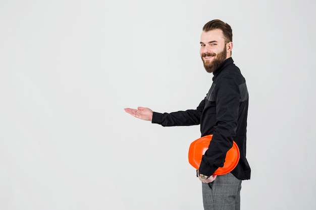 Smiling architect holding bright hardhat presenting against white backdrop